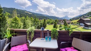 An outdoor patio with wicker furniture and a table, overlooking a mountainous landscape with houses. - Alpine's Nest studio apartment with mountain views (Kirchberg in Tirol)