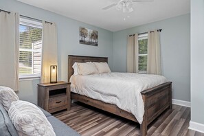 Un dormitorio con cama de madera, mesita de noche, lámpara y ventana con cortinas.
