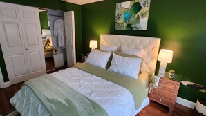 A bedroom with a bed, bedside tables, a dresser, a mirror, and a green wall.