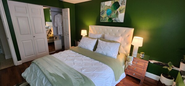 A bedroom with a bed, bedside tables, a dresser, a mirror, and a green wall.