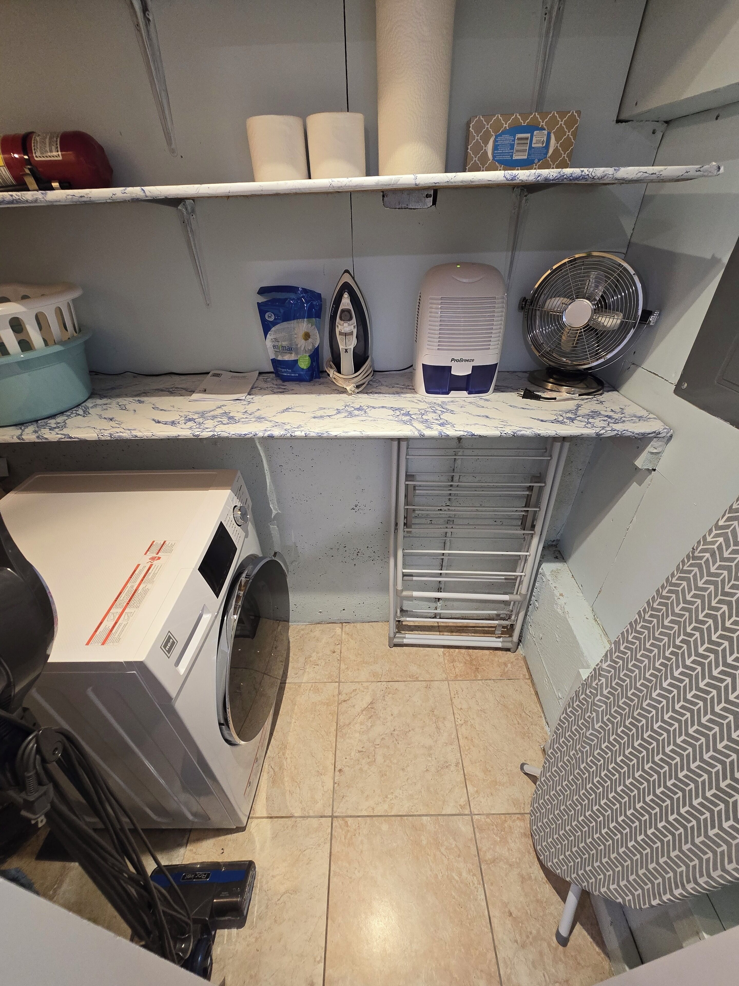 Ein Waschraum mit Waschmaschine, Bügeleisen, Ventilator und Ablagefläche mit Handtüchern und Wäschekorb.