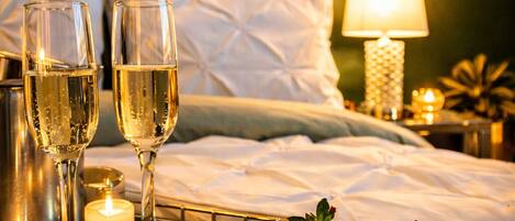 A neatly arranged bedroom with a bed, bedside table, and a tray with chocolate-covered strawberries and champagne glasses.