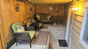 A wooden-floored patio with wicker furniture, a small table with a vase of flowers, and decorative wall art.
