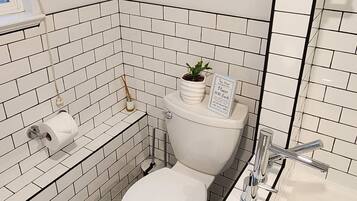 Et badeværelse med hvide flisevægge, et gulv med et sort-hvidt mønster, et toilet, en vask og et badekar.