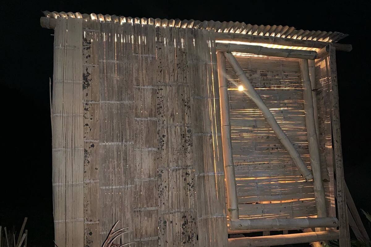 A rustic wooden structure with a corrugated roof and a door illuminated by interior lighting.