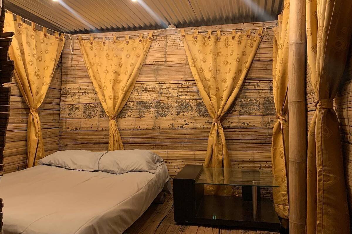 A room with a bed, a glass-top table, and curtains tied back.