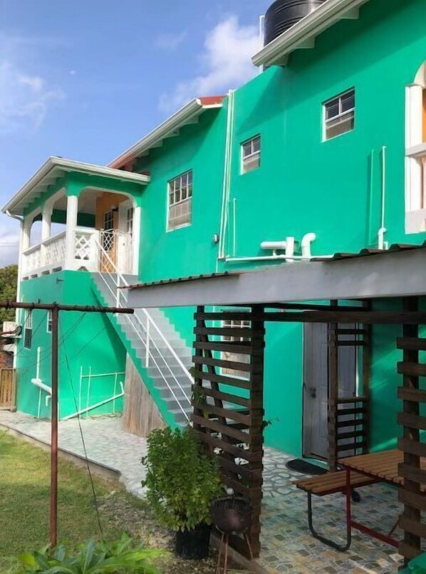 Una casa de dos pisos con fachada verde, un balcón en el nivel superior y una escalera que conduce a la entrada.