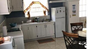 A compact kitchen with white cabinets, a refrigerator, a sink, and a dining area with a table and chairs.