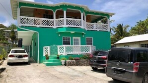 A two-story house with a green exterior and white balconies. There are two cars parked in front.