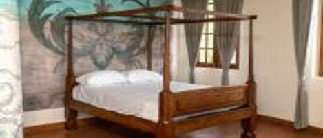 A four-poster bed in a room with a mural on the wall and a ceiling fan.