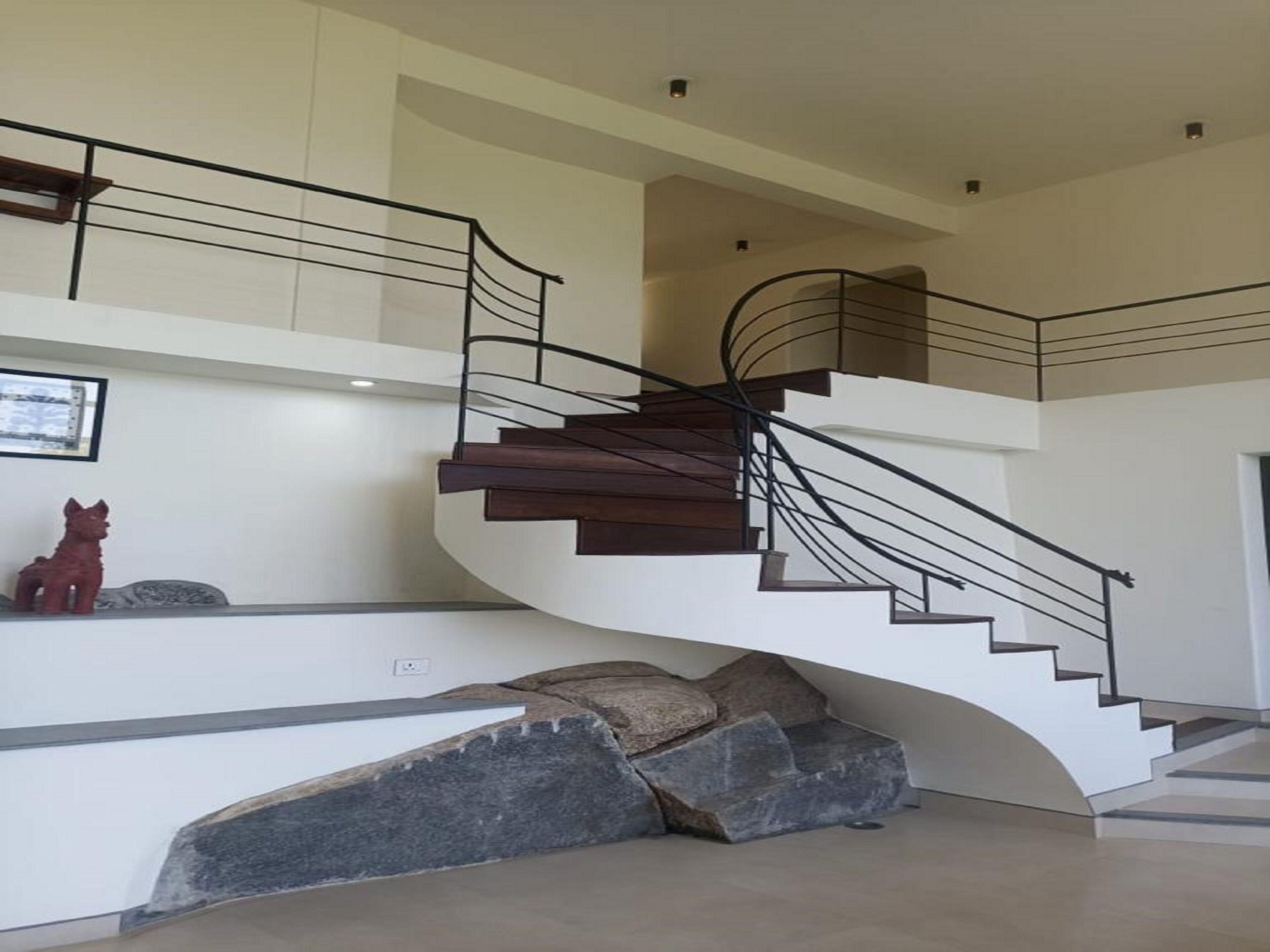 A modern staircase with a curved design, black railings, and a stone accent wall.