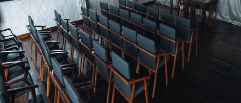 A conference room with rows of chairs, a wooden table, and large windows with curtains.