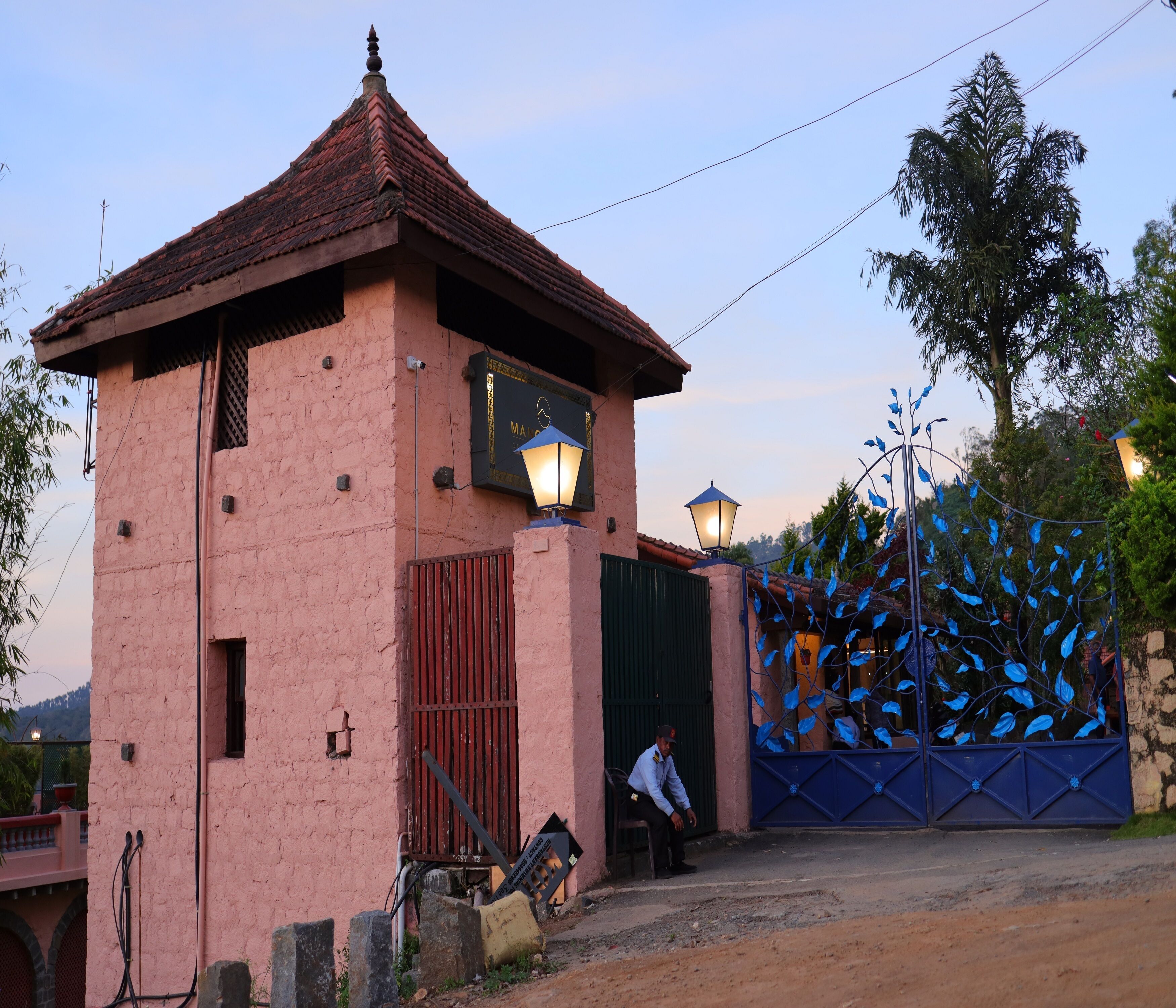 A pink building with a tiled roof, a sign reading "MAIRIE," and a blue decorative gate.