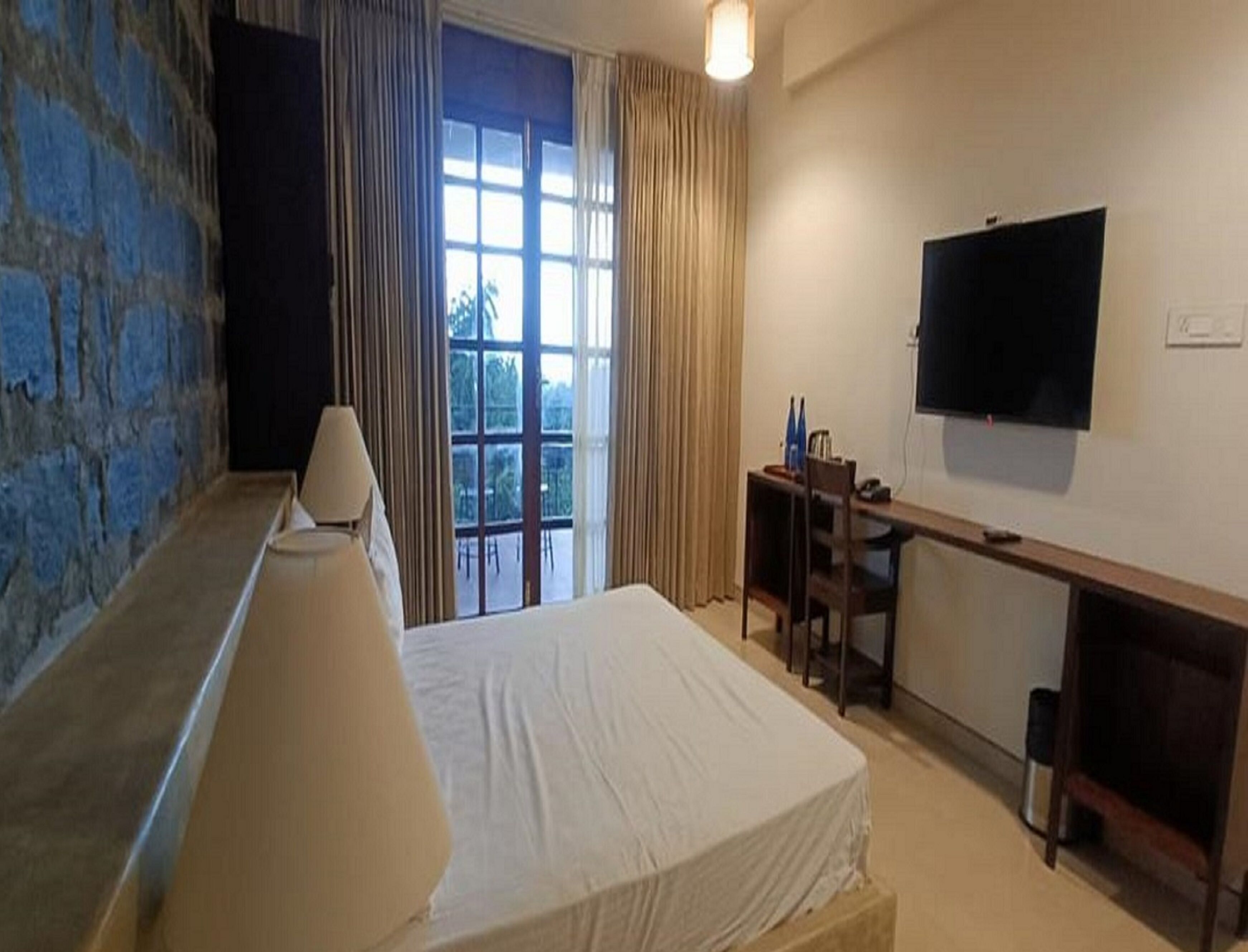 A hotel room with a bed, a desk, a chair, a television, and a window with curtains.