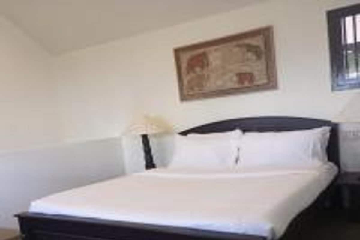 Ein ordentlich bezogenes Bett mit weißen Leinen in einem schlichten Zimmer, das ein dunkles Holz-Kopfteil hat.