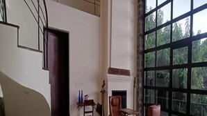 A spacious room with a large window, a fireplace, and a staircase leading to an upper level. - Mango Hill Yercaud (Yercaud)