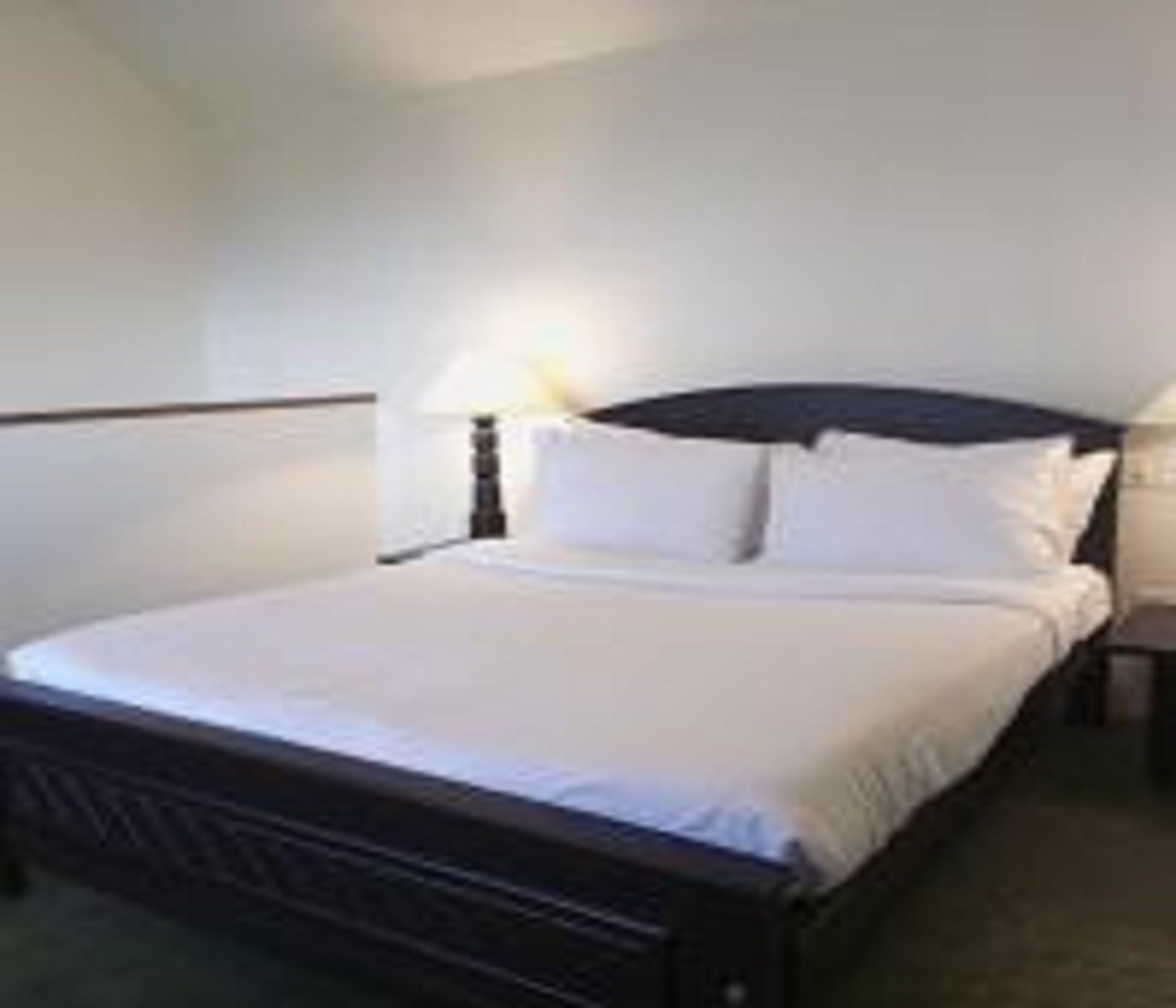 A neatly made bed with white linens in a hotel room.