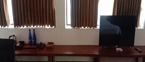 A room with a wooden desk, a television, and curtains on the windows.