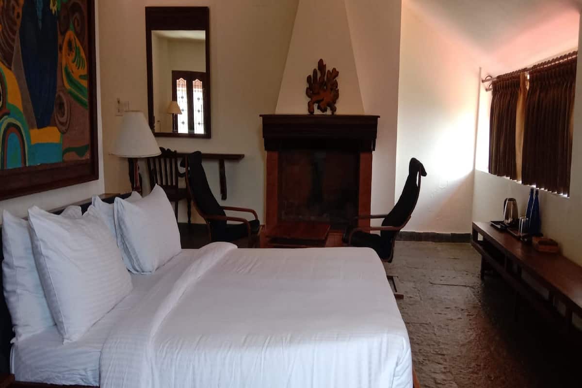 Ein Schlafzimmer mit einem großen Bett, einem Holzkapillon, einem Sessel, einem Spiegel und einem Kamin.