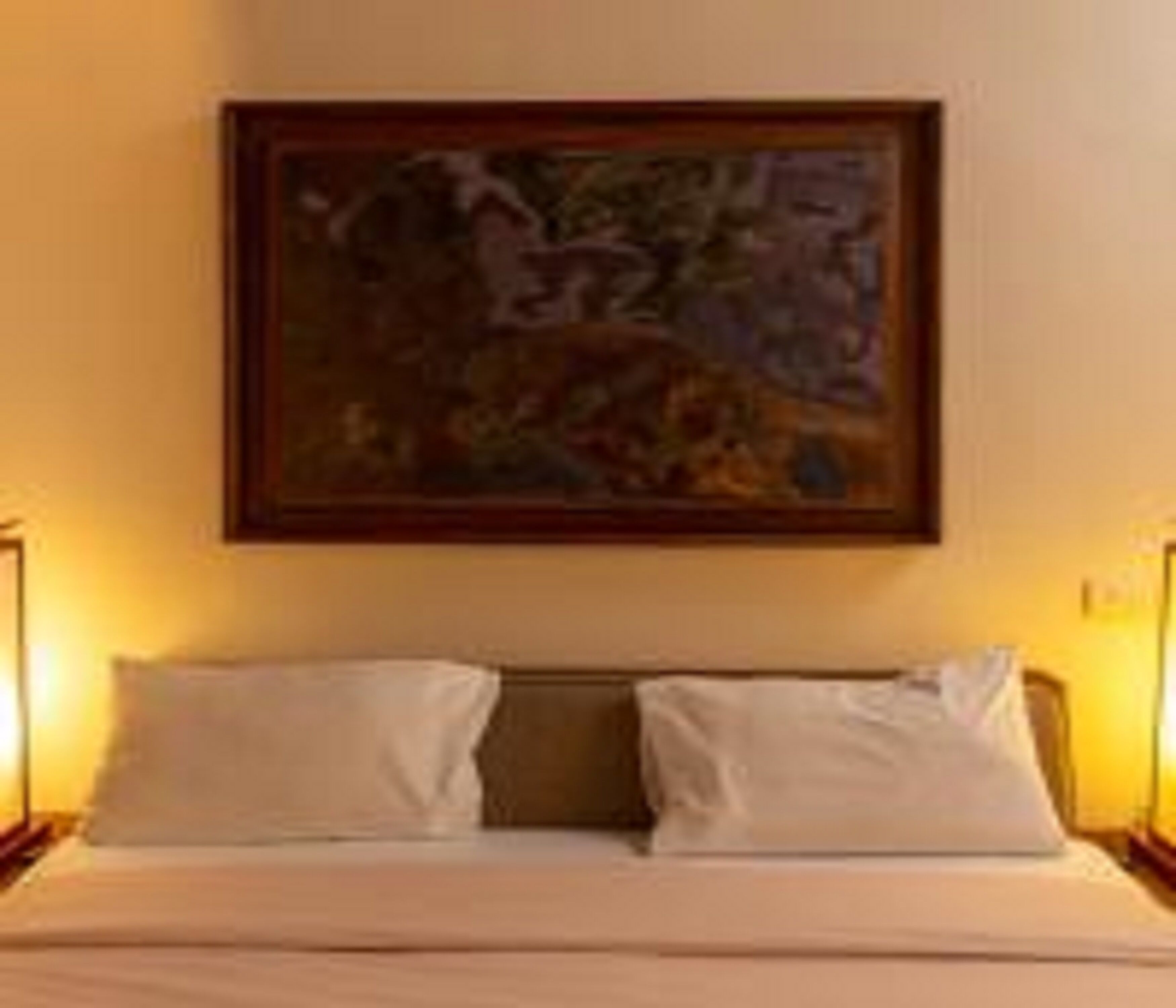 Una habitación de hotel con cama, dos almohadas, un cuadro en la pared y dos lámparas de noche.