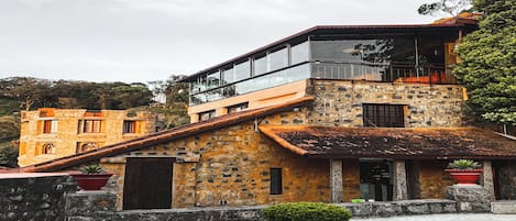 A multi-story stone building with a mix of traditional and modern architectural elements, including a balcony and a glass enclosure.