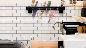 A kitchen with a white tiled backsplash, a black utensil holder with colorful utensils, a microwave, and a wooden cabinet. - Cozy Modern Place with Projector @ Near Pink Church (Thành phố Hồ Chí Minh)