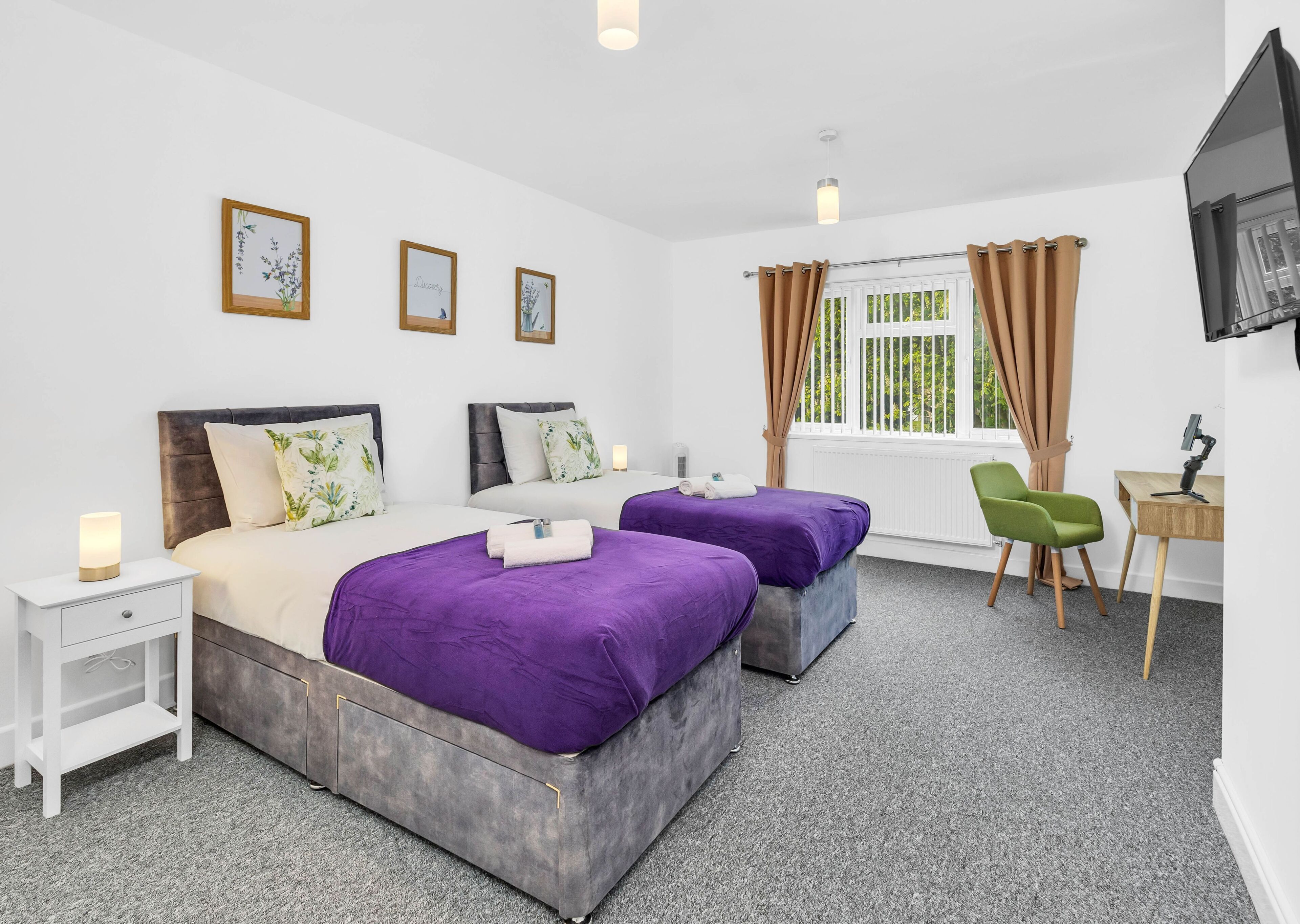 A hotel room with two beds, a desk, a chair, and a TV.