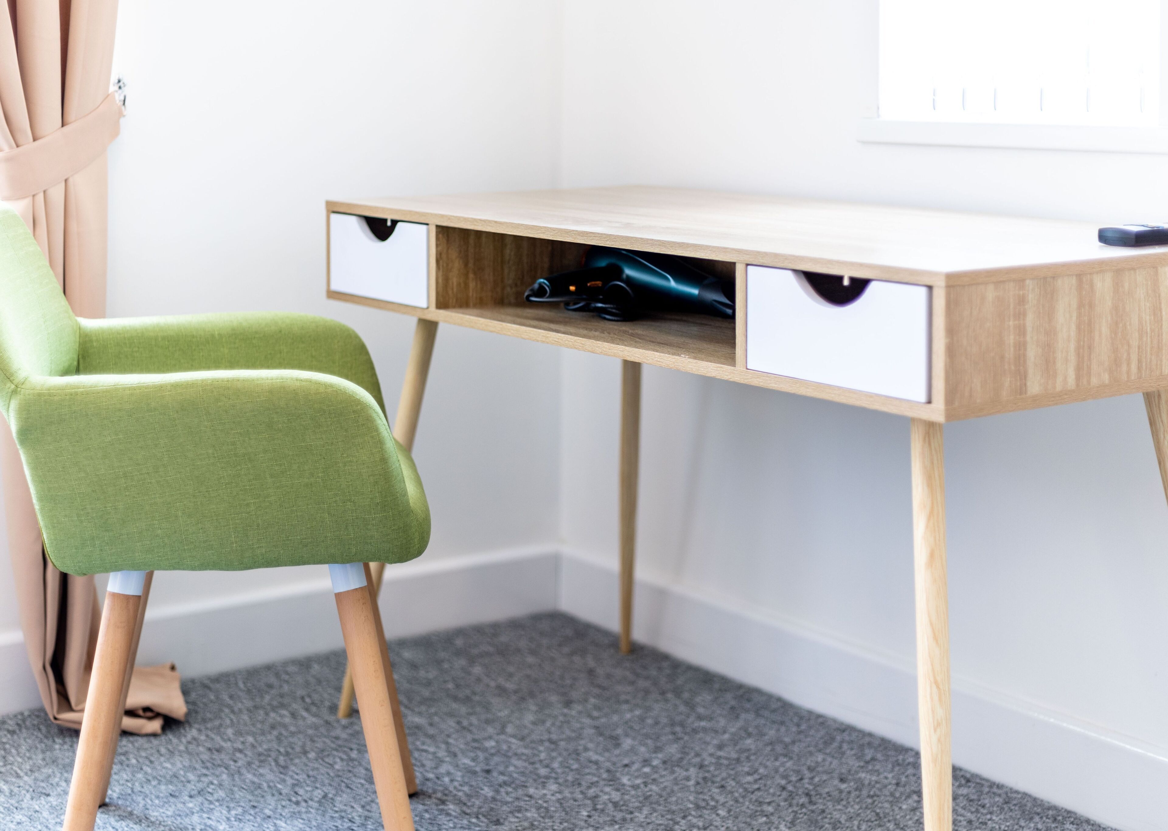 A corner desk with a green chair, wooden legs, and a grey carpet.