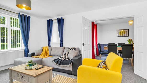 Una sala de estar moderna con un sofá, un sillón amarillo, una mesa de centro y una zona de comedor al fondo.