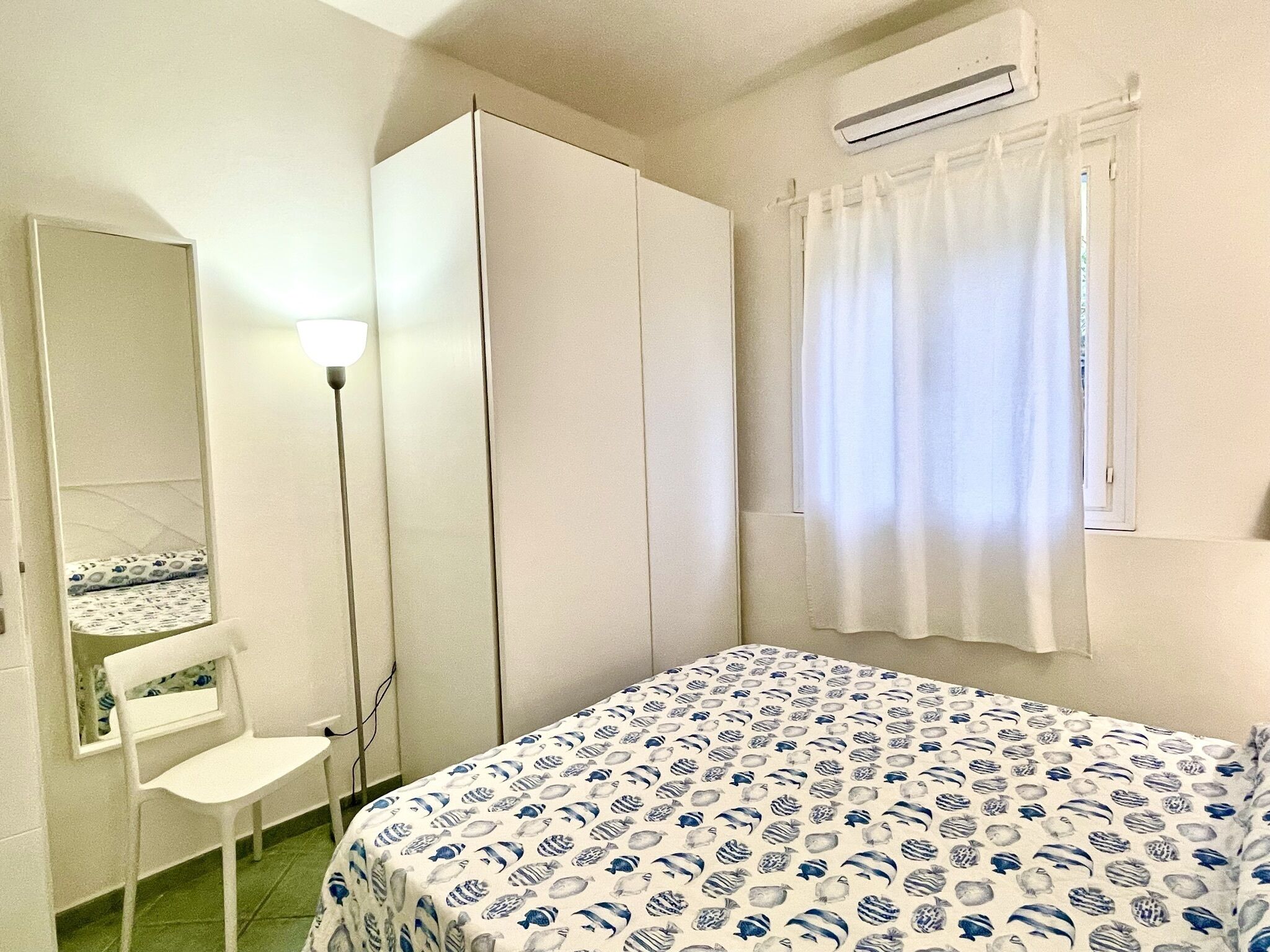A bedroom with a bed, a wardrobe, a chair, and an air conditioning unit.