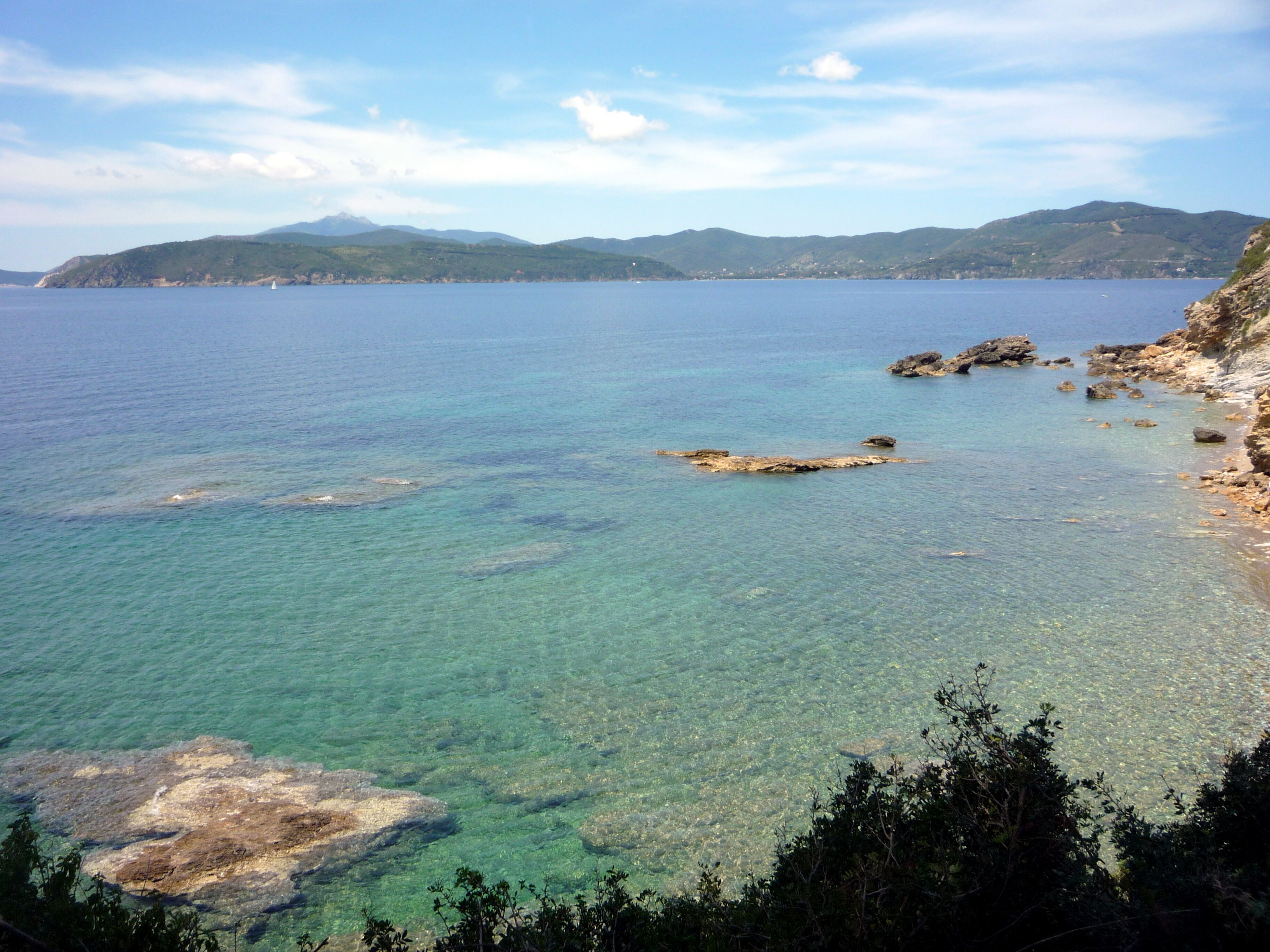 Un paysage côtier caractérisé par des eaux limpides, des rivages rocheux et des montagnes lointaines.