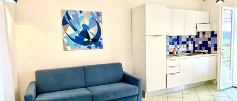 A modern kitchen with white cabinets, a blue tiled backsplash, and a blue sofa in a living area.