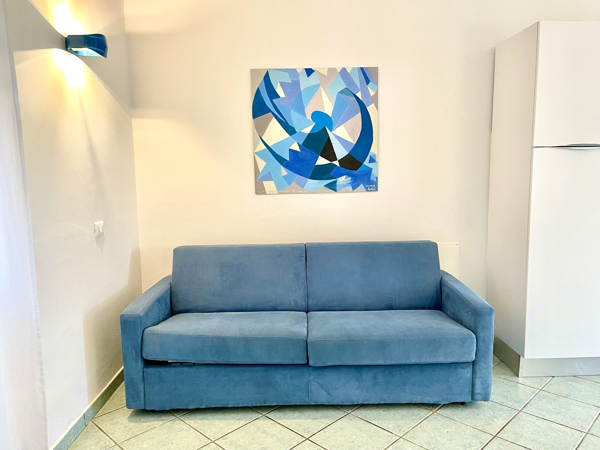 A blue sofa in a room with a white wall and a geometric painting.
