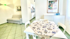 A dining area with a table set for two, a sofa, and a kitchen in the background. - Les Bouganvilles by SolturElba (Capoliveri)