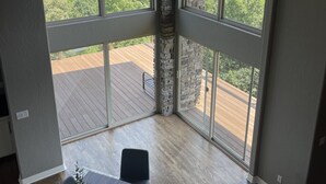 Een ruime kamer met grote ramen en uitzicht op een houten terras en groen.