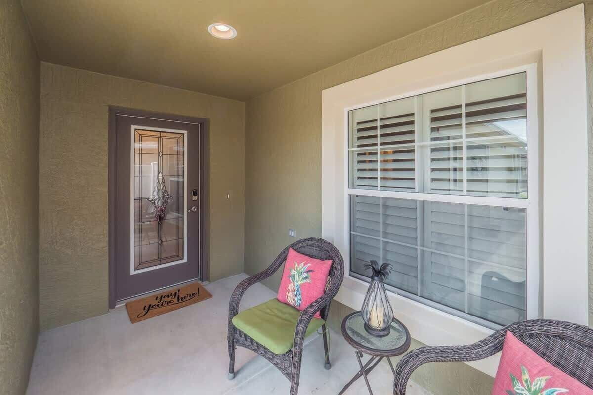 A room with a door, a window with blinds, wicker chairs, and a small table with a vase.