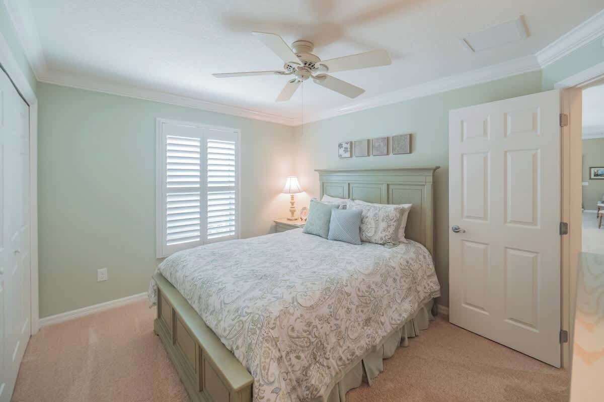 A bedroom with a bed, a ceiling fan, a nightstand with a lamp, and a door.