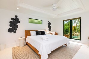 A modern bedroom with a large bed, a view of a tropical landscape, and a unique wall art installation.