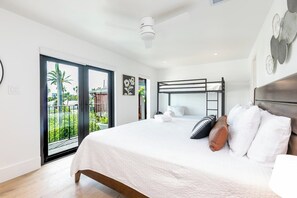 A bedroom with a bunk bed, a balcony with a view of palm trees, and a ceiling fan.