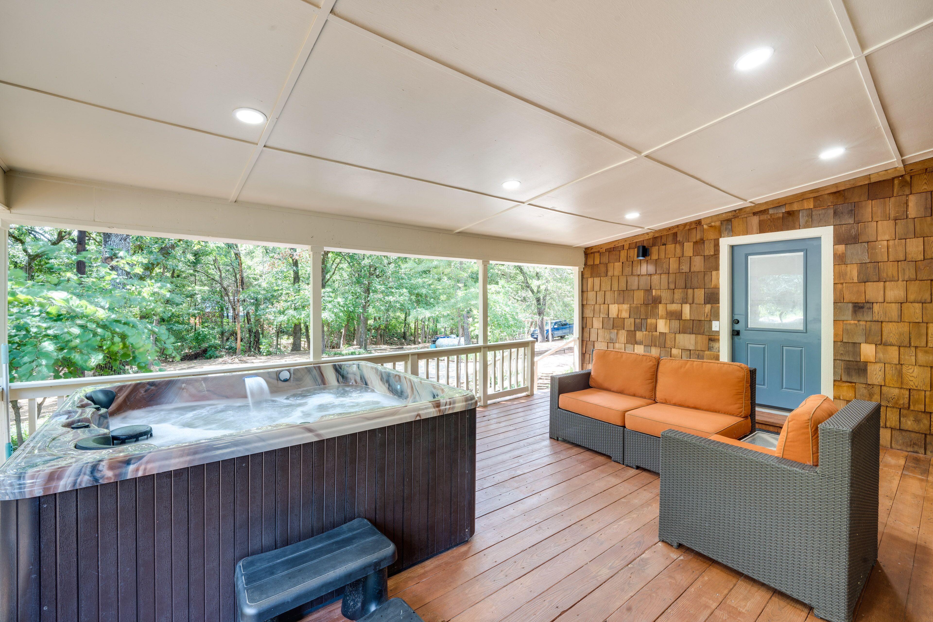 Un espacio al aire libre cubierto con un jacuzzi, mobiliario de mimbre y vistas de la vegetación circundante.