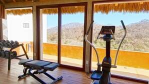 A gym with exercise equipment and large windows overlooking a mountainous landscape. - Beautiful Condo with Private Beach Club (Cruz de Huanacaxtle)