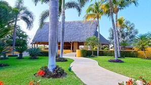 A resort with a thatched-roof building, surrounded by palm trees and well-maintained lawns. - Beautiful Condo with Private Beach Club (Cruz de Huanacaxtle)