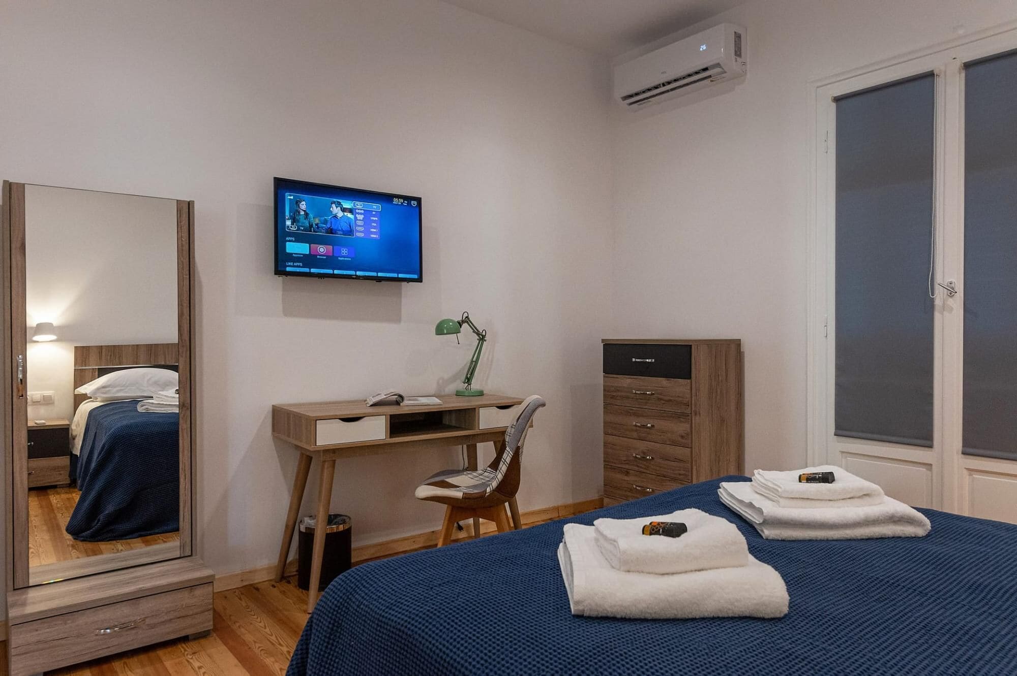 Ein Hotelzimmer mit Bett, Schreibtisch mit Stuhl, Wandfernseher und Kleiderschrank.