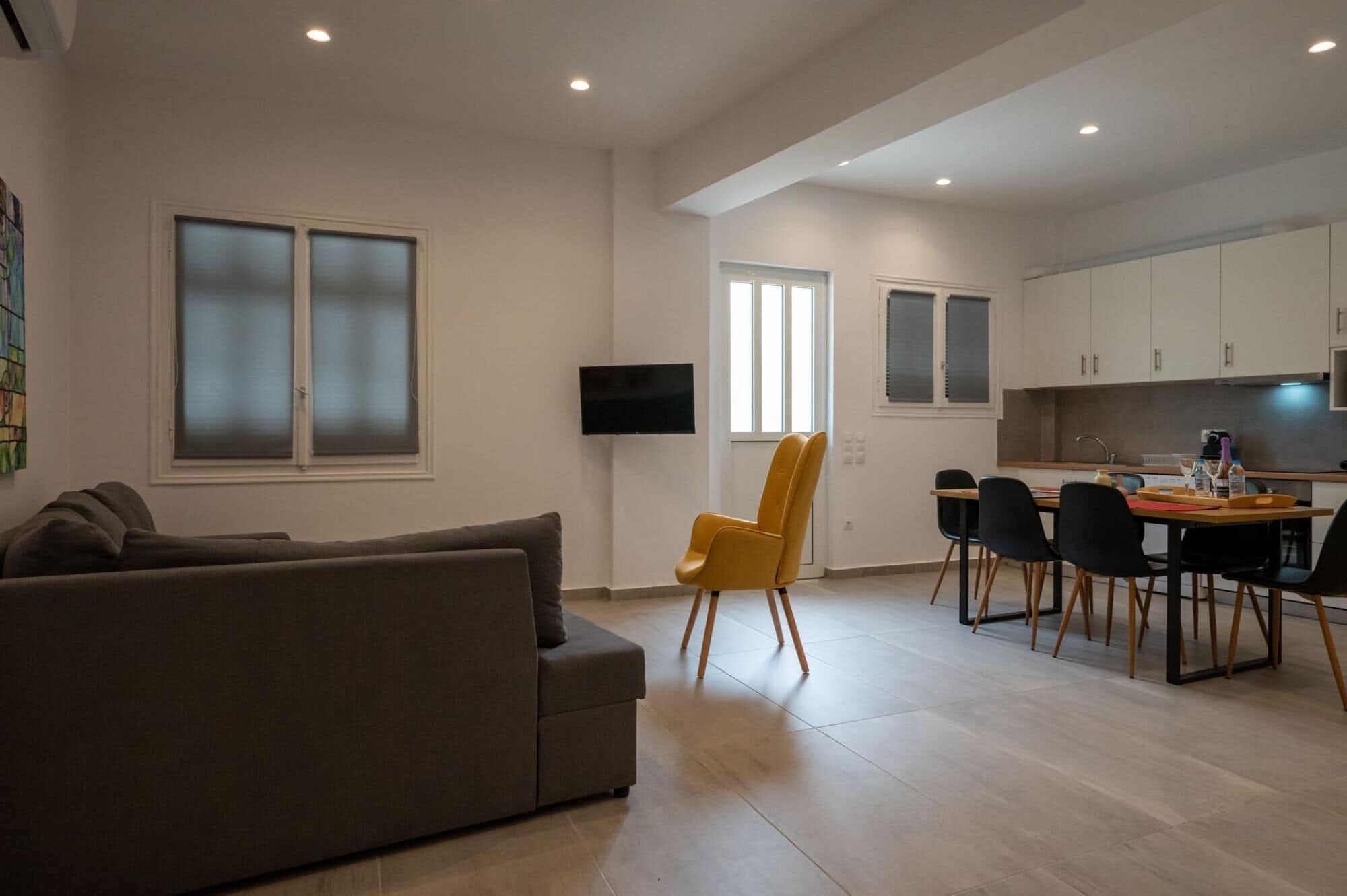 A modern living room with a sofa, a yellow chair, and a dining area with a table and chairs.