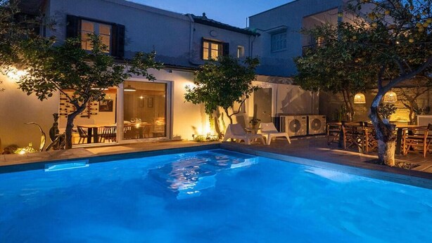 Une piscine entourée d’arbres et de bâtiments, avec des chaises longues et des tables.