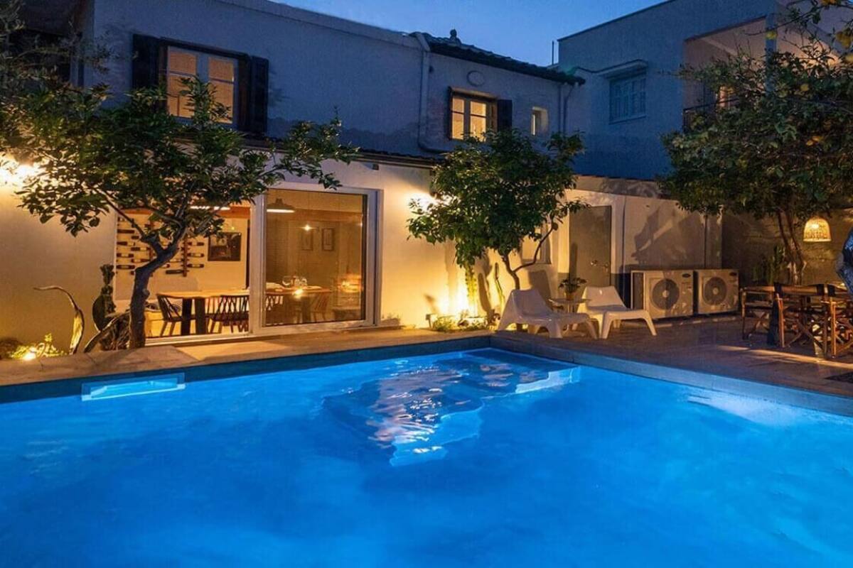 Une piscine entourée d’arbres et de bâtiments, avec des chaises longues et des tables.