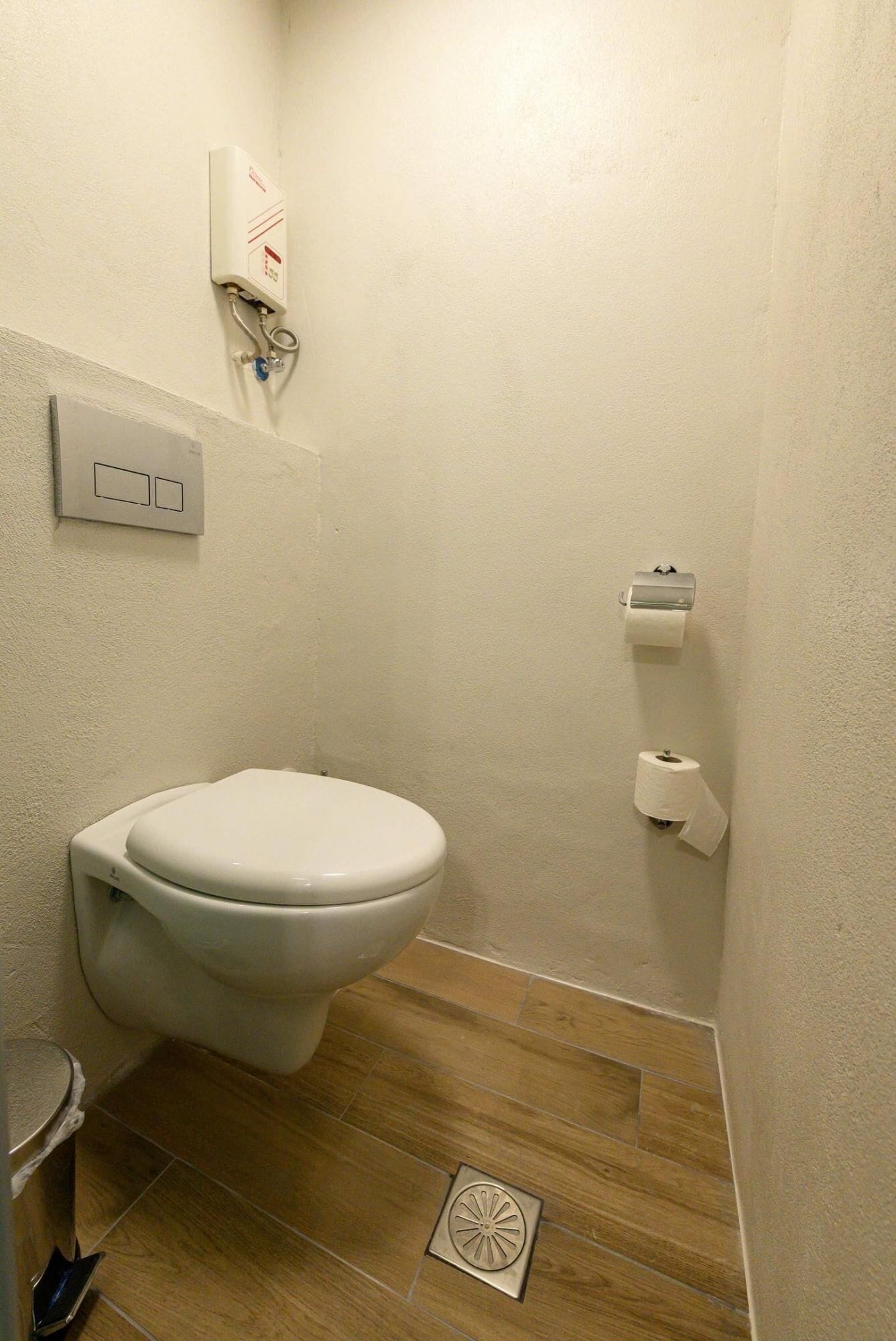 Un baño pequeño con inodoro, un dispensador de papel higiénico en la pared y un desagüe en el suelo.