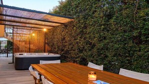 Une terrasse extérieure accueillante, avec une table et des chaises en bois, un jacuzzi et une pergola en bambou.