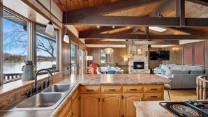 A kitchen with wooden beams, a large island, and a view of a lake. - Cedar Lake getaway - sauna, paddle boards & raft! (Annandale)