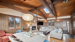 A spacious living area with a fireplace, a large dining table, and a cozy seating arrangement. - Cedar Lake getaway - sauna, paddle boards & raft! (Annandale)